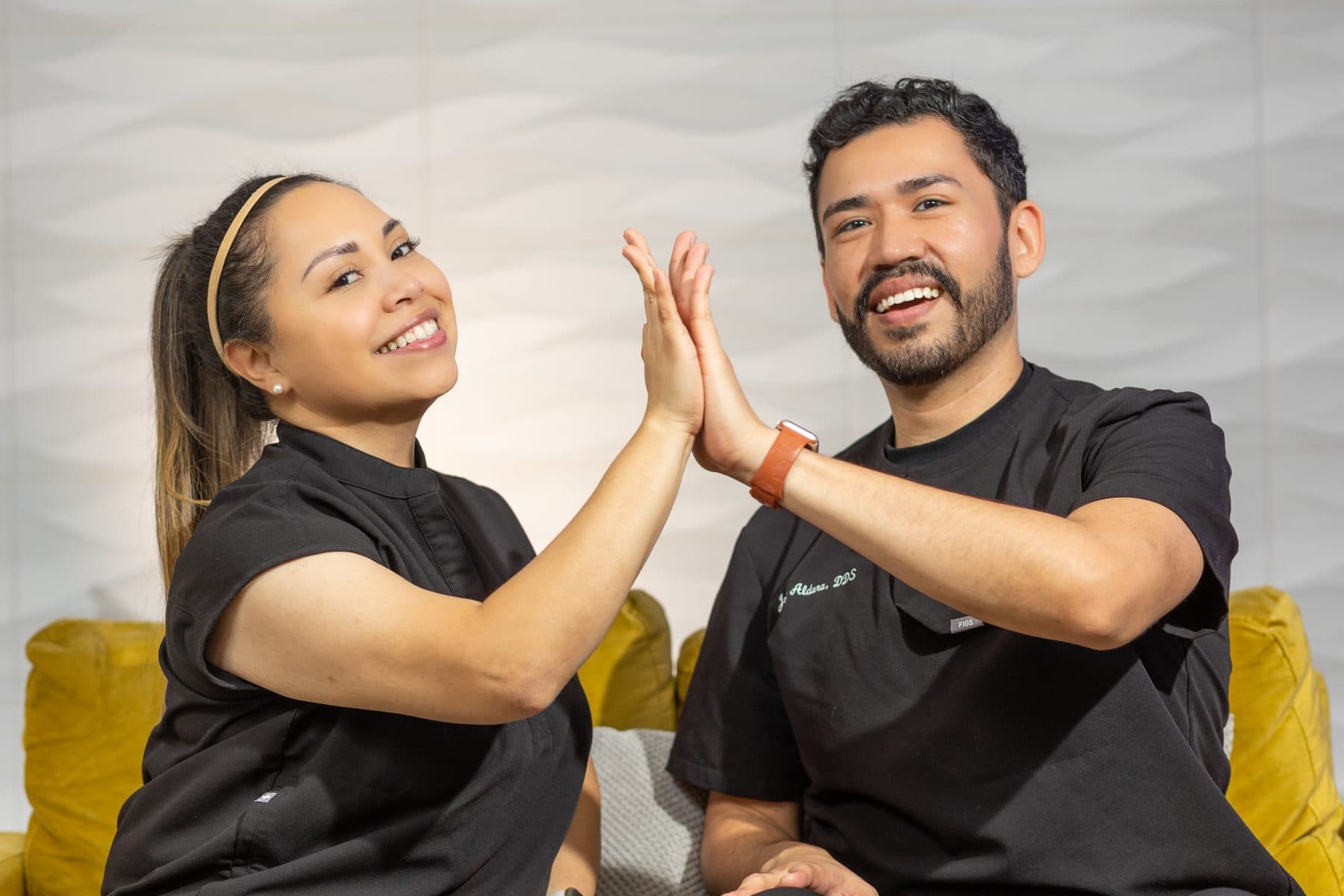 Dr. Jose Aldana and Dr. Diana Vazquez high-fiving on the yellow sofa