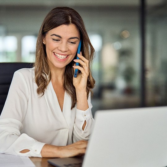 Smiling woman talking on phone and working on laptop