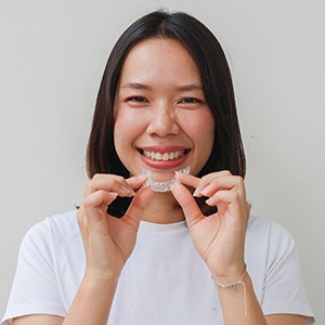 Woman smiling while holding clear aligner