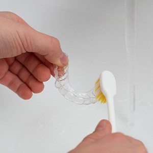 Patient using toothbrush to clean aligner
