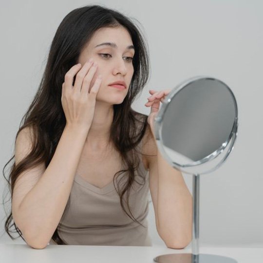 Woman looking at herself in mirror, concerned about signs of aging