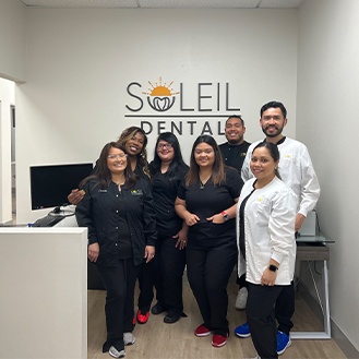 Dental team smiling in front of Soleil Dental logo