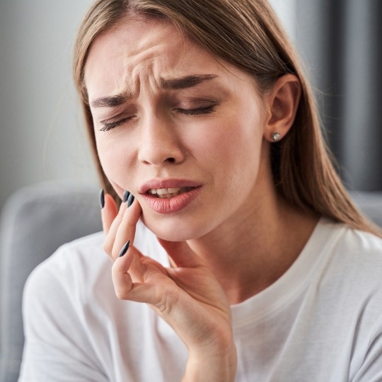 Woman holding cheek in pain before emergency dentistry