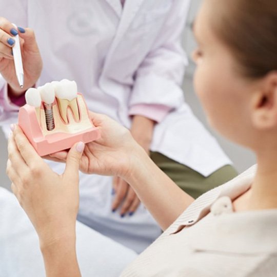 Dentist showing patient model of dental implant in Dallas
