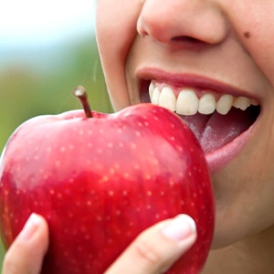 Woman with dental implants in Dallas, TX eating an apple