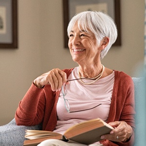 Senior woman with dental implants in Dallas, TX reading on couch