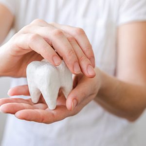 Person holding a large plaster model of a tooth