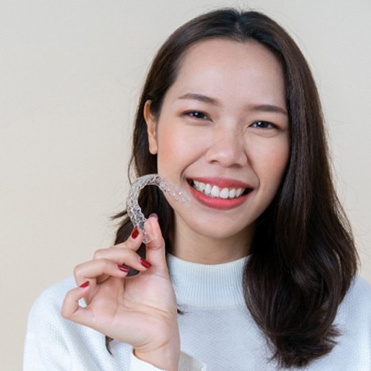 patient smiling while holding Invisalign aligner