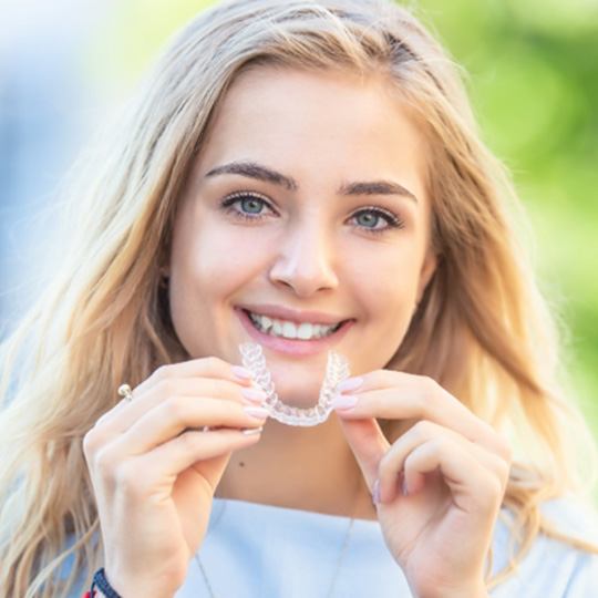 patient smiling while holding Invisalign aligner