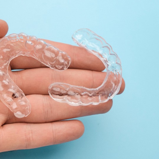 closeup of person holding two Invisalign clear aligners