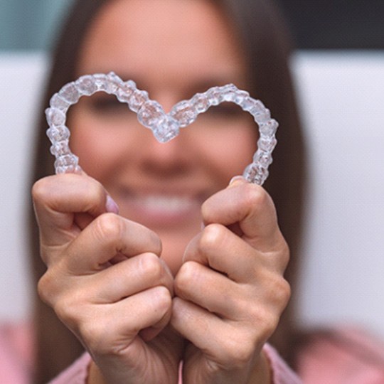 Woman holding Invisalign aligners in the shape of a heart