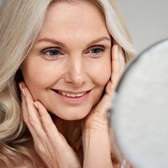 woman with long gray hair smiling at mirror