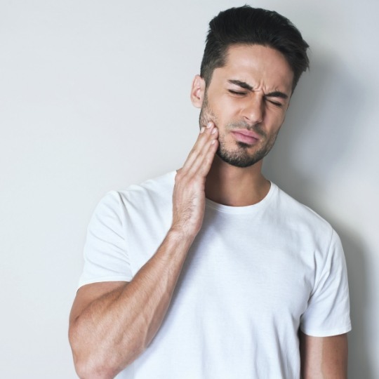 Man holding jaw in pain before wisdom tooth extractions