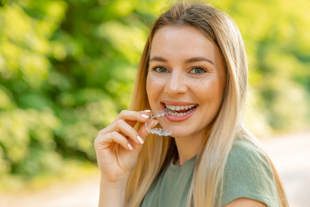 Smiling woman with blonde hair holding Invisalign outside