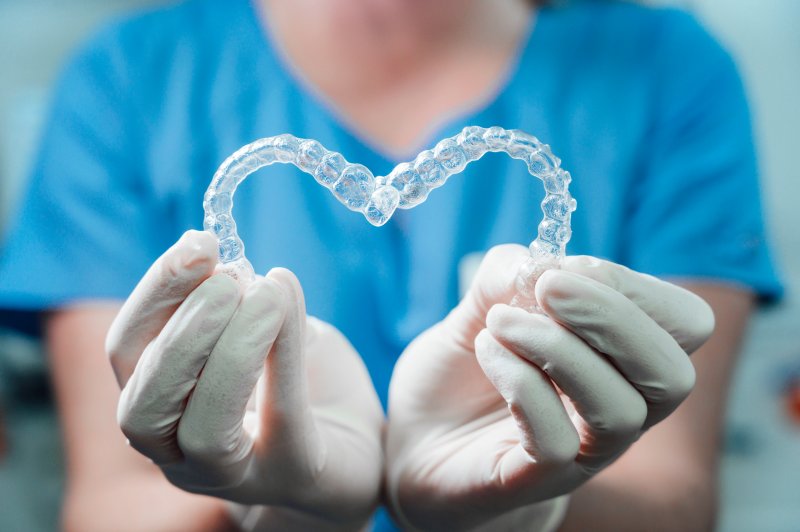 A dentist holding up two Invisalign aligners in the shape of a heart