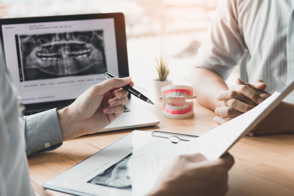 Hands of dentist and patient at desk with X-rays and treatment plan